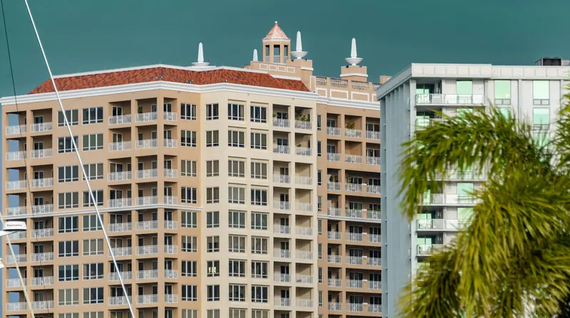 Mid-rise condominium towers with balconies and a palm tree on the Florida coast